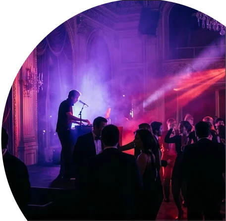 Un DJ mixant sur scène lors d'une soirée animée avec des projecteurs de lumière rose et violette et des gens qui dansent dans une salle de réception élégante
